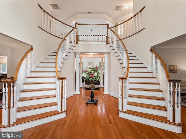 stairway featuring ornate columns, ornamental molding, a towering ceiling, and hardwood / wood-style floors