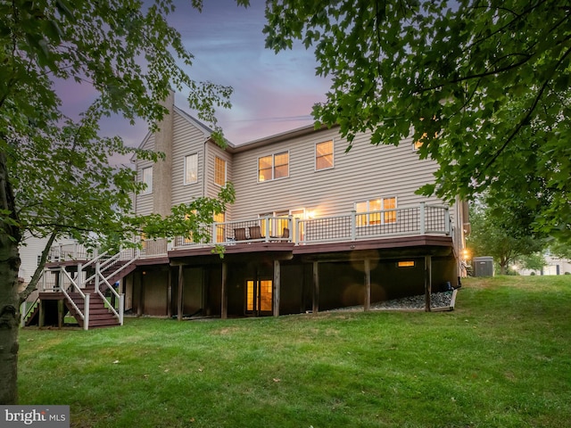 back house at dusk featuring a deck and a lawn