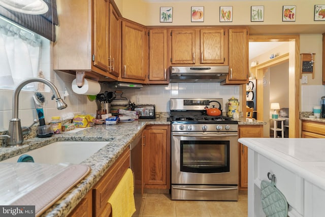 kitchen with light stone counters, light tile patterned floors, sink, stainless steel gas range, and decorative backsplash