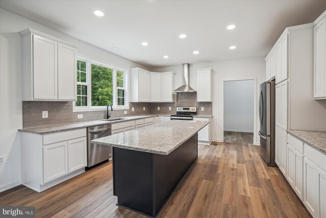 kitchen with wall chimney range hood, hardwood / wood-style floors, sink, light stone countertops, and appliances with stainless steel finishes