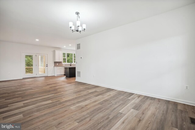 unfurnished living room with an inviting chandelier, sink, and light hardwood / wood-style floors