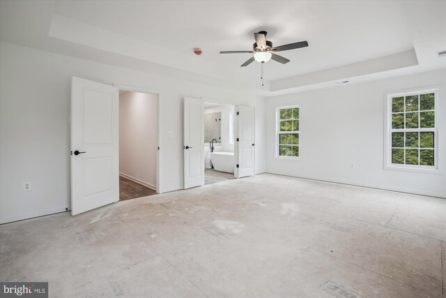 unfurnished bedroom with ceiling fan, ensuite bathroom, and a tray ceiling