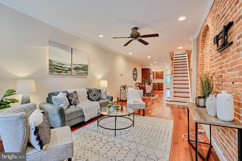 living room with crown molding, wood-type flooring, ceiling fan, and brick wall