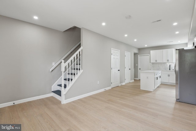 kitchen with tasteful backsplash, white cabinets, stainless steel fridge, light hardwood / wood-style floors, and a center island