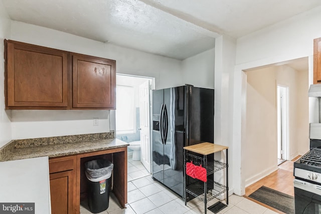 kitchen with black fridge, light tile patterned flooring, exhaust hood, and stainless steel range with gas cooktop