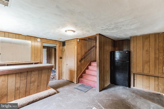 basement with wooden walls and black refrigerator