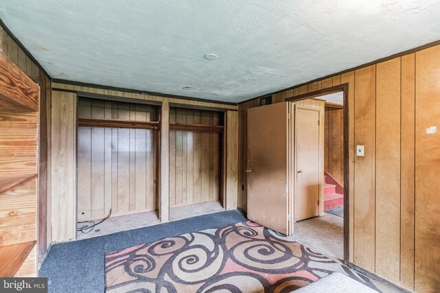 interior space with light colored carpet, wooden walls, and a textured ceiling