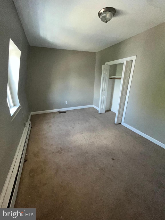 unfurnished bedroom featuring a baseboard radiator, a closet, and carpet floors