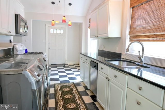 kitchen featuring dark floors, appliances with stainless steel finishes, white cabinetry, a sink, and separate washer and dryer