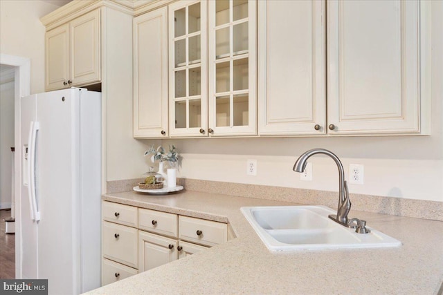 kitchen with white refrigerator with ice dispenser, sink, cream cabinetry, and light stone counters