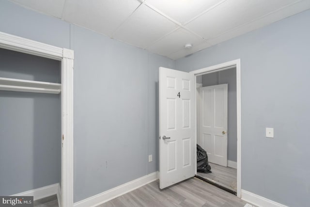 unfurnished bedroom with a drop ceiling, light wood-type flooring, and a closet