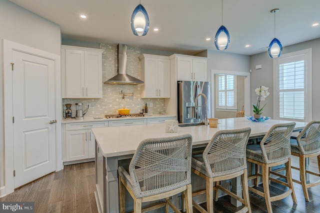 kitchen with wall chimney exhaust hood, white cabinetry, and an island with sink