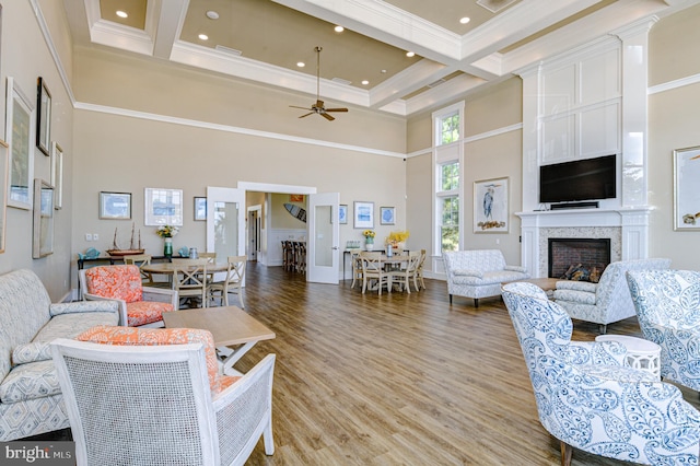 living room featuring ceiling fan, beamed ceiling, a high ceiling, crown molding, and light hardwood / wood-style flooring