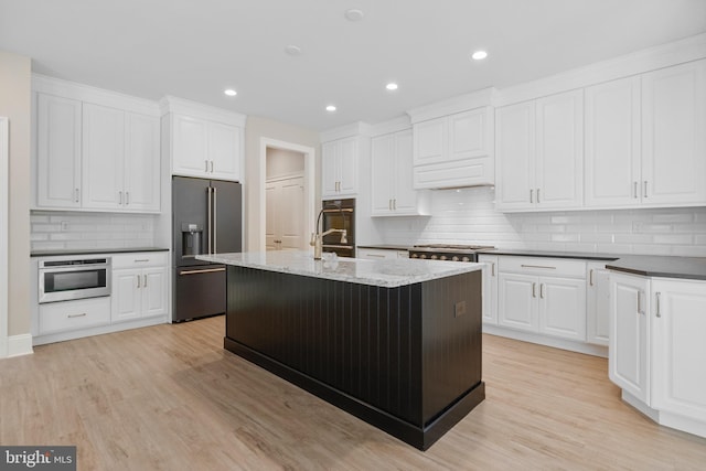 kitchen featuring an island with sink, light stone counters, white cabinets, and high end fridge