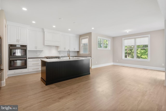 kitchen with a sink, a center island with sink, dobule oven black, and white cabinets