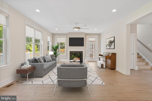 living room featuring a warm lit fireplace, recessed lighting, visible vents, stairs, and light wood finished floors