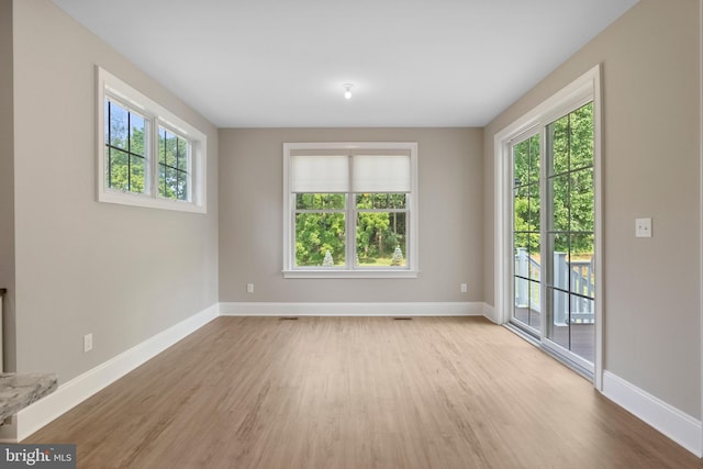 unfurnished room featuring plenty of natural light, light wood-style flooring, and baseboards