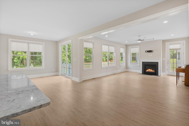 unfurnished living room with light wood-type flooring, a fireplace with flush hearth, baseboards, and a wealth of natural light