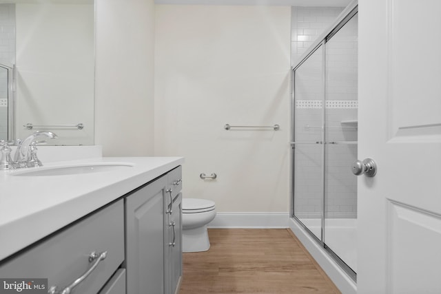 bathroom with toilet, wood finished floors, vanity, baseboards, and a shower stall