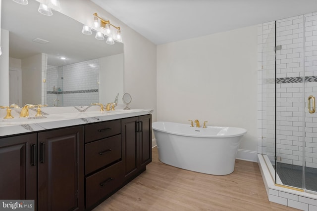 full bath with a freestanding tub, a sink, wood finished floors, a shower stall, and double vanity