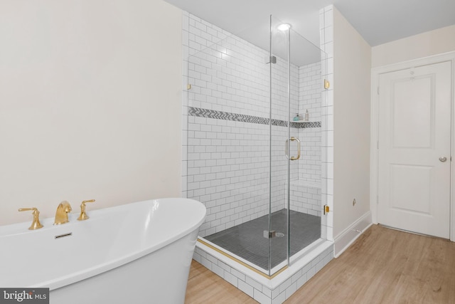 bathroom featuring a stall shower, a freestanding bath, baseboards, and wood finished floors