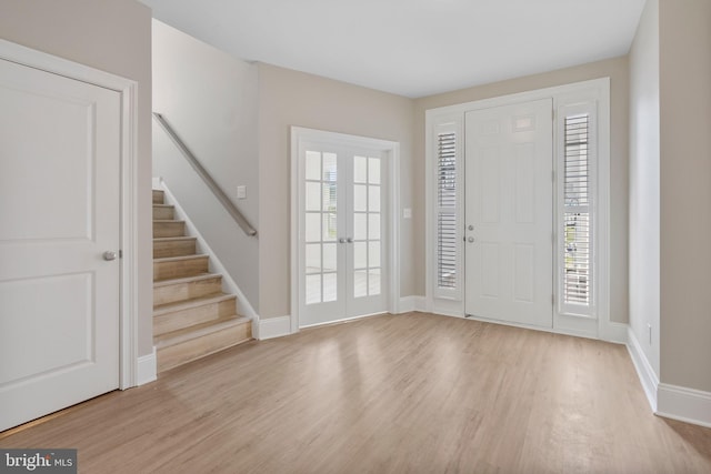 foyer with light wood-style flooring, french doors, stairway, and baseboards