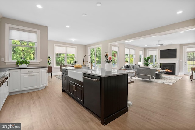 kitchen with light stone counters, a center island with sink, stainless steel dishwasher, open floor plan, and a sink