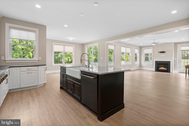 kitchen featuring open floor plan, a kitchen island with sink, a sink, light stone countertops, and dishwasher