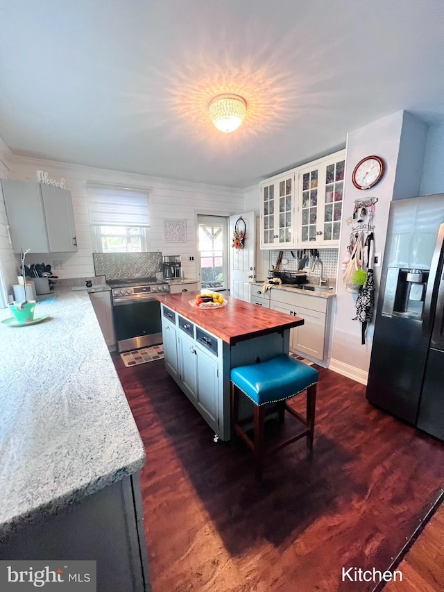 kitchen with stainless steel range with electric stovetop, refrigerator with ice dispenser, butcher block countertops, tasteful backsplash, and dark hardwood / wood-style flooring