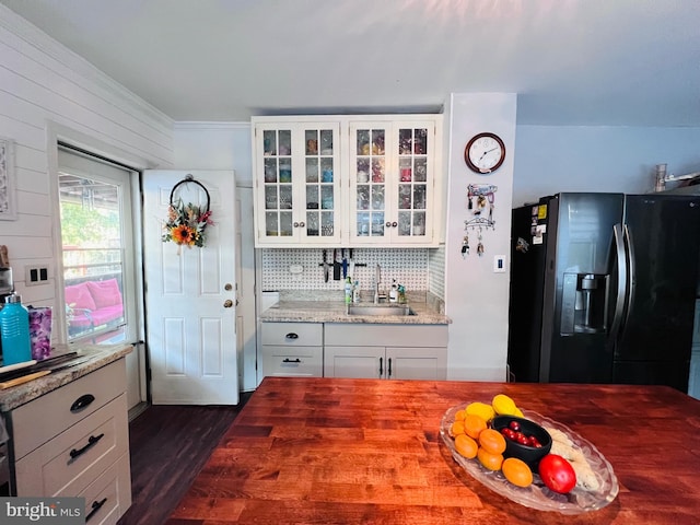 kitchen with tasteful backsplash, black fridge, light stone counters, sink, and dark wood-type flooring