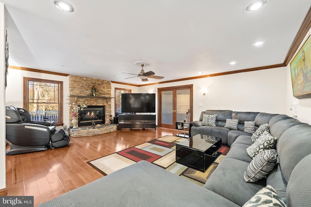 living room with ceiling fan, a stone fireplace, hardwood / wood-style flooring, and ornamental molding