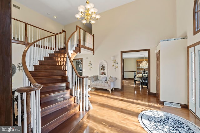 stairway with a towering ceiling, a notable chandelier, and wood-type flooring