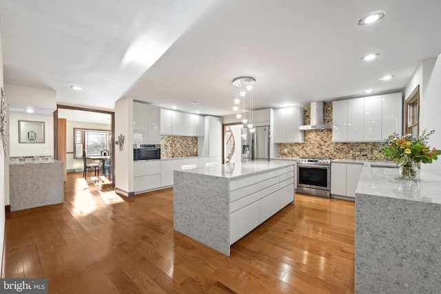 kitchen featuring light hardwood / wood-style flooring, white cabinetry, appliances with stainless steel finishes, wall chimney exhaust hood, and a kitchen island