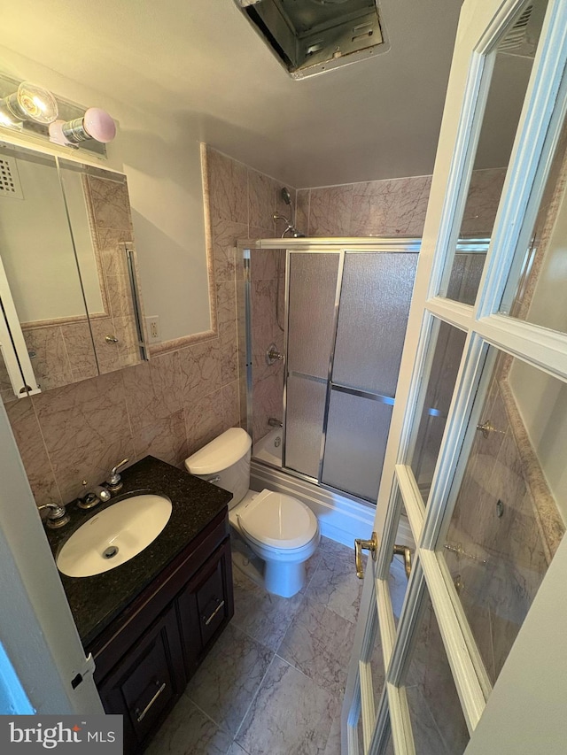 full bathroom with vanity, toilet, combined bath / shower with glass door, and tile walls