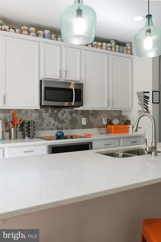 kitchen with hanging light fixtures, sink, white cabinetry, and light stone counters