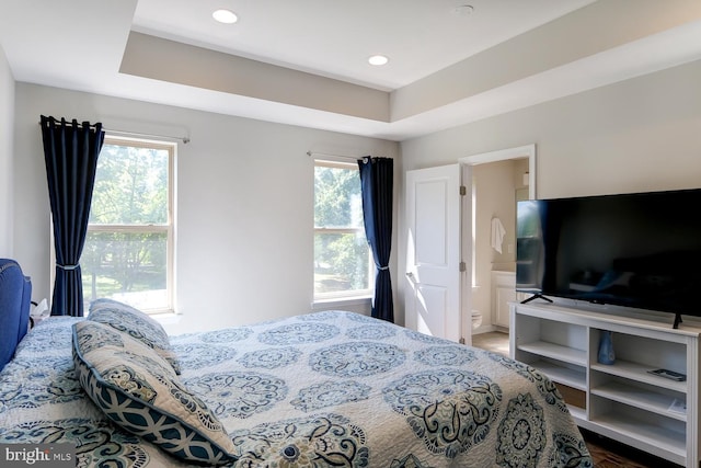 bedroom with a raised ceiling, hardwood / wood-style flooring, multiple windows, and ensuite bath