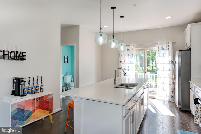 kitchen with white cabinetry, stainless steel fridge, sink, and an island with sink