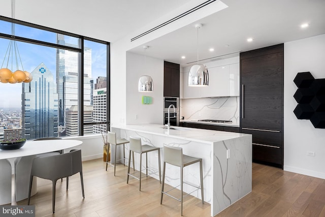 kitchen featuring decorative backsplash, light wood-style floors, a sink, modern cabinets, and a kitchen breakfast bar