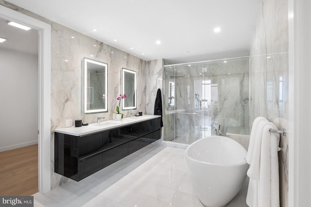 full bathroom featuring tile walls, a marble finish shower, double vanity, a freestanding bath, and a sink