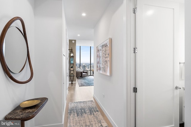 corridor featuring baseboards, light wood-type flooring, and recessed lighting