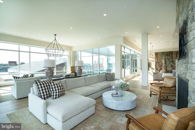 living room with a notable chandelier, light hardwood / wood-style flooring, and a stone fireplace