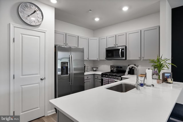 kitchen featuring stainless steel appliances, sink, light hardwood / wood-style floors, gray cabinetry, and kitchen peninsula