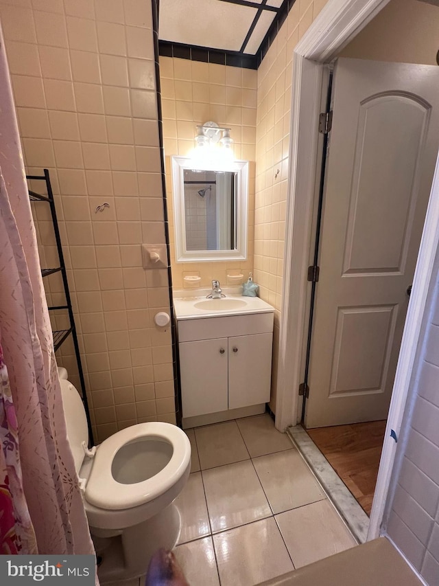 bathroom with toilet, vanity, tile patterned flooring, and tile walls