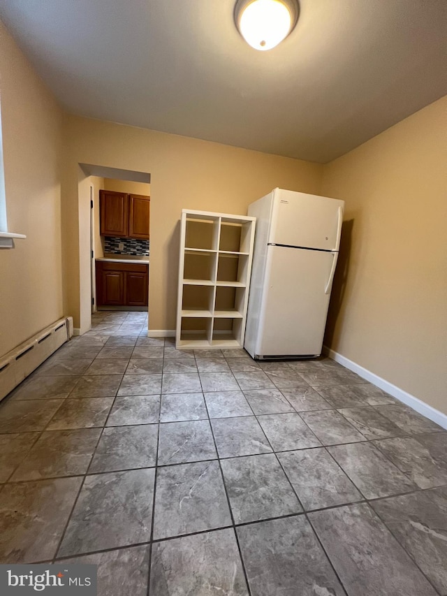 unfurnished bedroom featuring a baseboard heating unit, white fridge, a closet, and light tile patterned floors