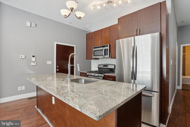 kitchen with sink, hardwood / wood-style flooring, appliances with stainless steel finishes, light stone countertops, and a center island with sink