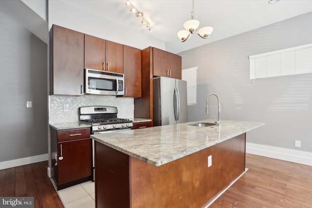 kitchen with appliances with stainless steel finishes, a center island with sink, sink, light hardwood / wood-style floors, and decorative backsplash