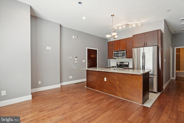 kitchen with stainless steel appliances, a center island with sink, pendant lighting, and light hardwood / wood-style flooring