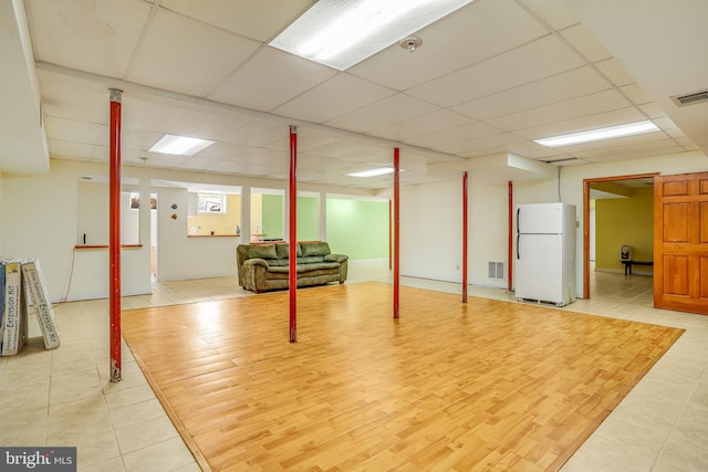 basement featuring a paneled ceiling, light hardwood / wood-style flooring, and white fridge