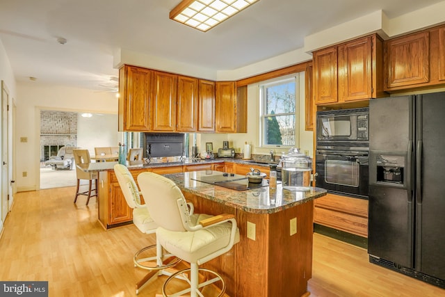 kitchen with a kitchen breakfast bar, dark stone counters, black appliances, light hardwood / wood-style flooring, and a fireplace