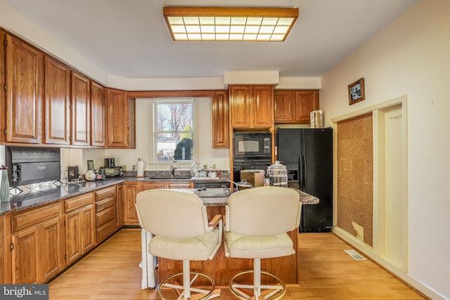 kitchen featuring dark stone counters, black appliances, a kitchen breakfast bar, sink, and light hardwood / wood-style floors